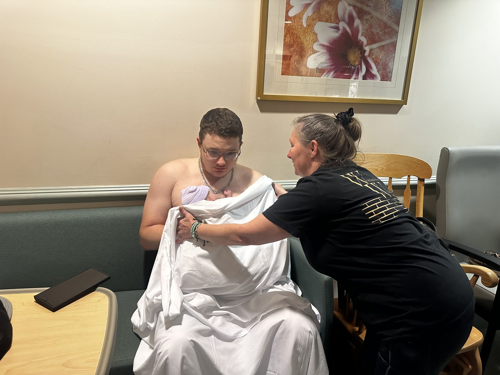 A new dad holding his newborn skin to skin in a hospital room while Kristie tucks a sheet around them both