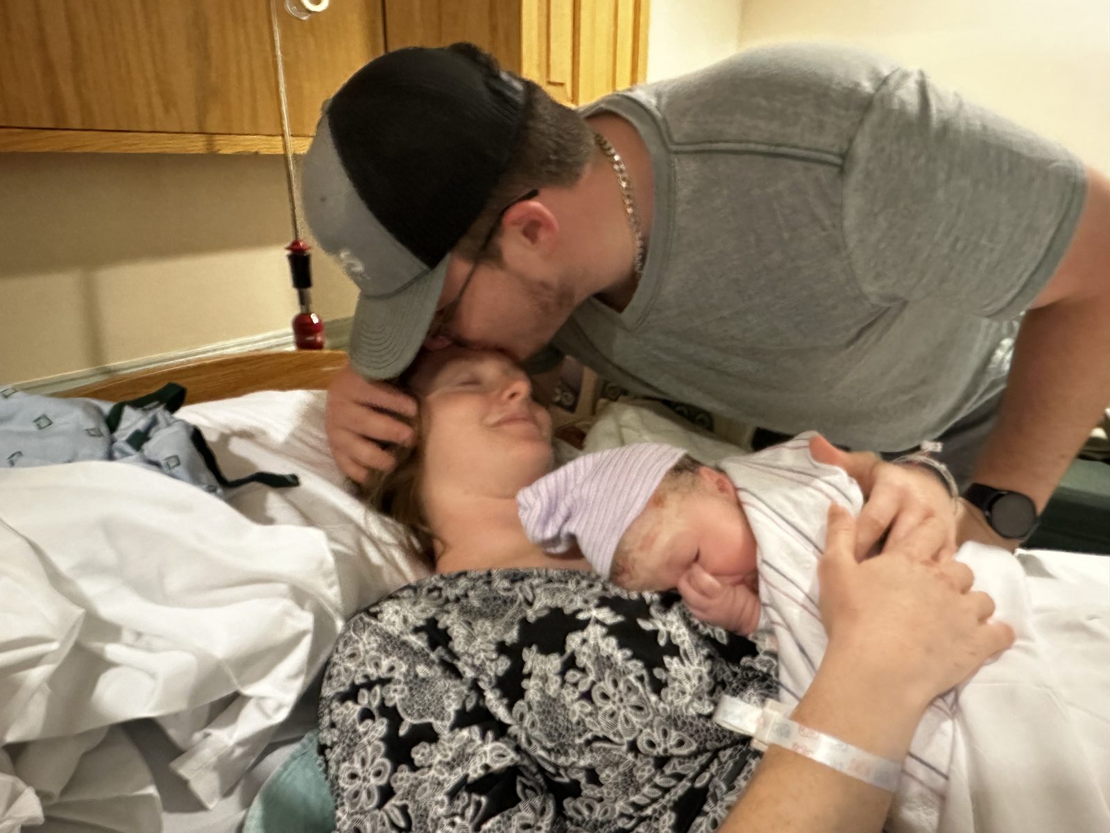 A dad kisses his wife’s forehead as she holds their just-born baby on her chest