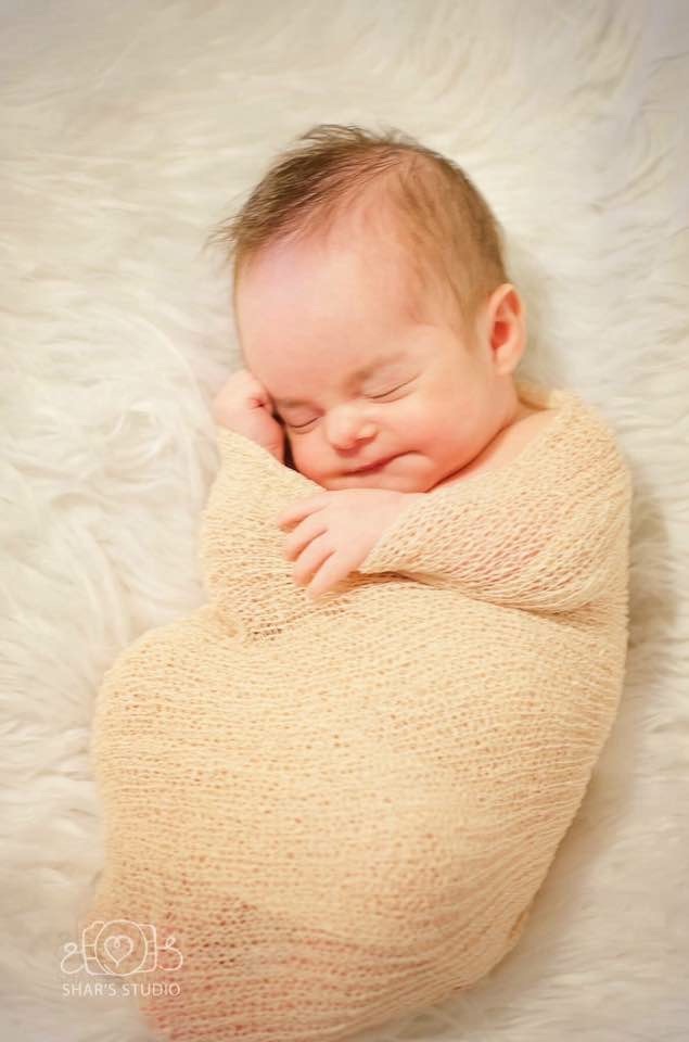 Baby Jeremiah asleep, swaddled on a soft white blanket